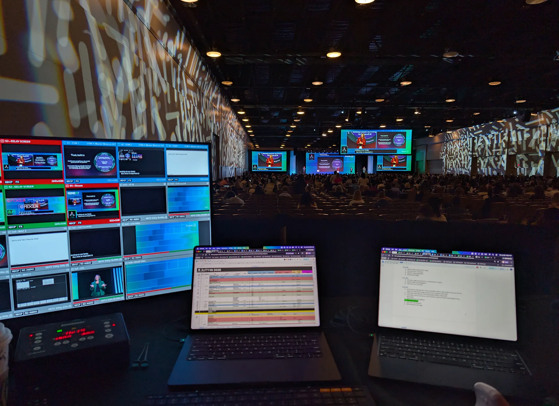 Behind-the-scenes production control station overlooking the Disability:IN Global Conference with monitors, laptops, and presentation screens.