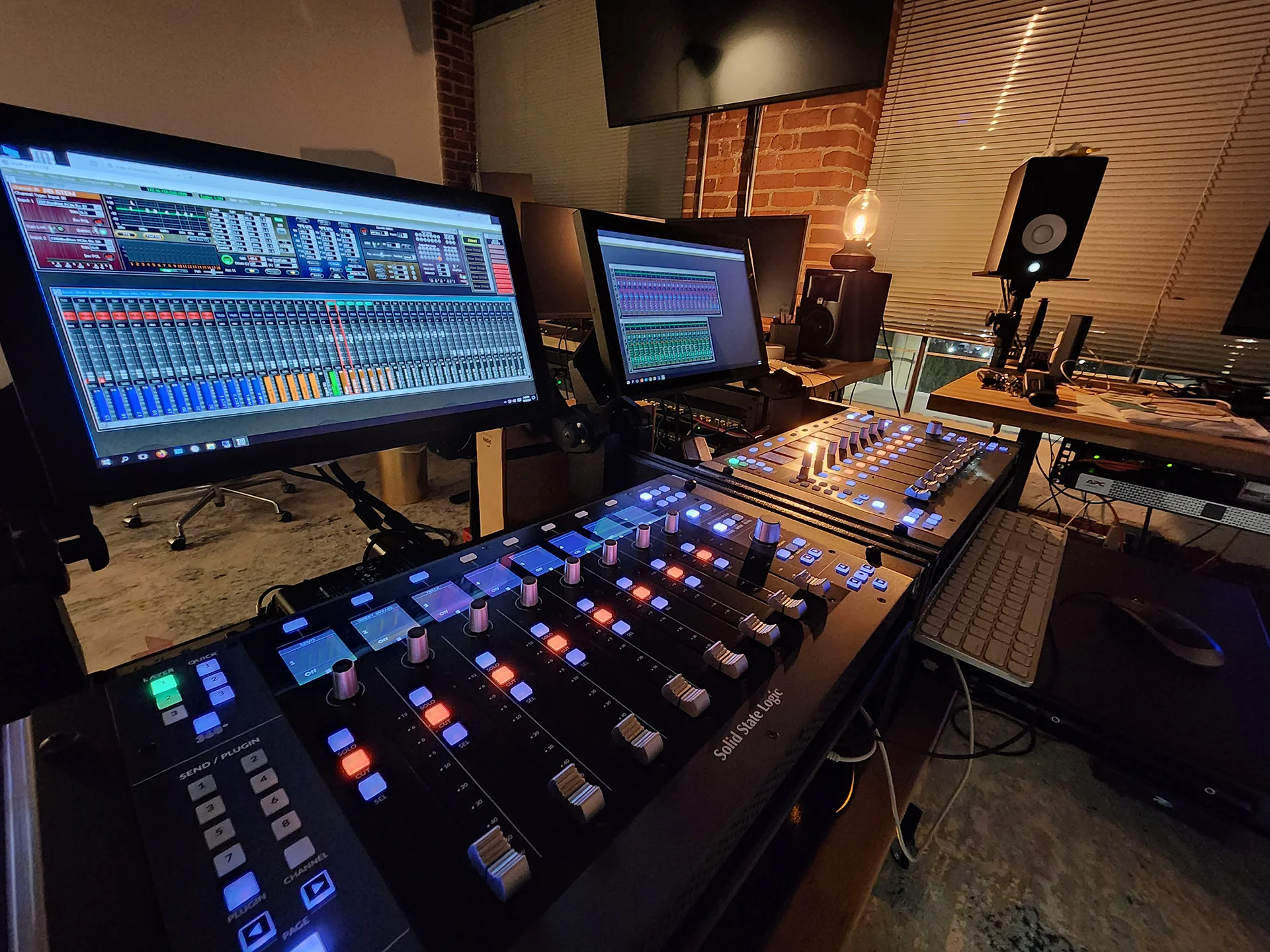 Protostream audio mixing consoles glow in a studio control room, with production software on nearby monitors.