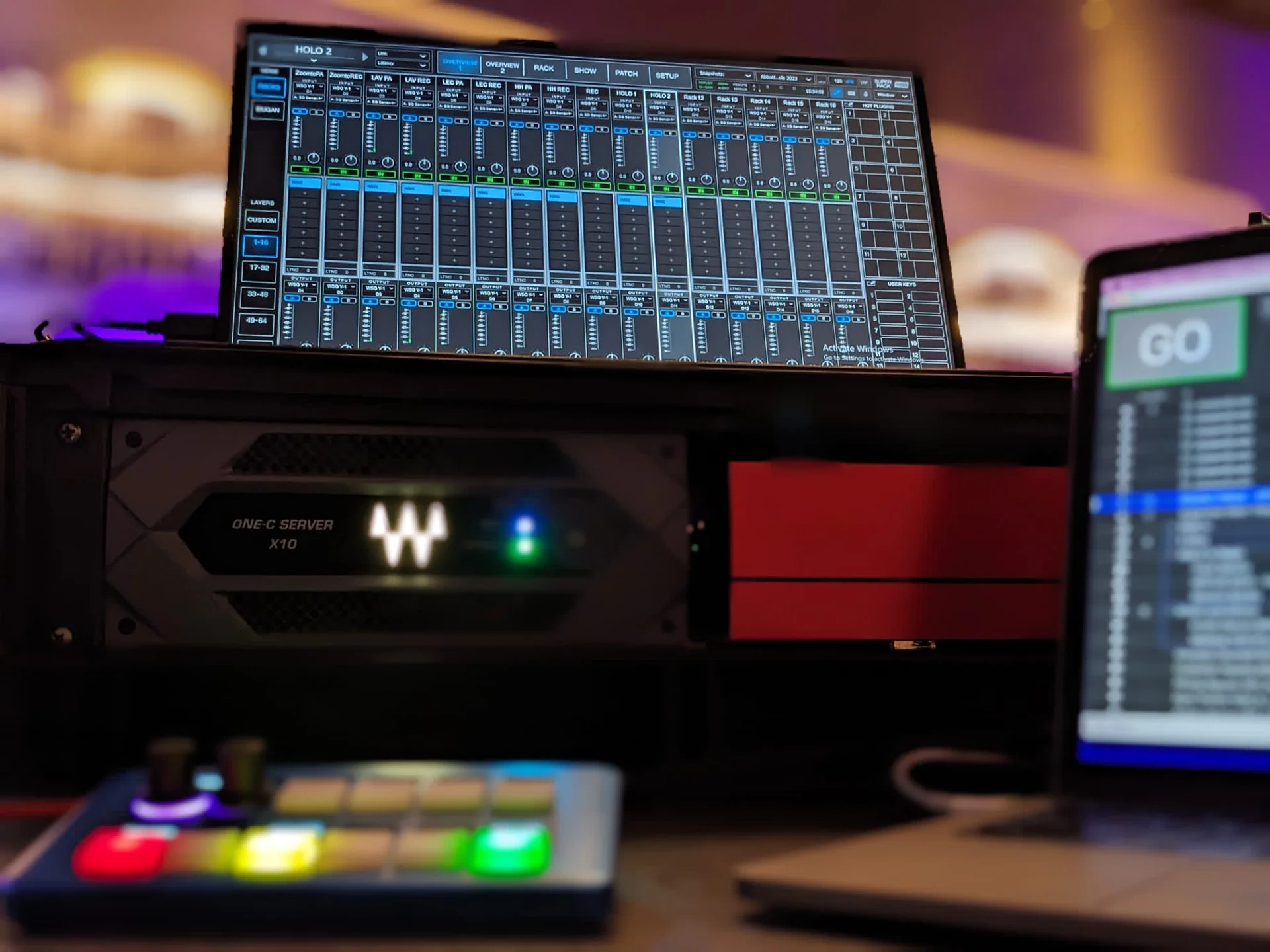 A Protostream digital mixing interface is displayed above rack-mounted audio equipment in a production studio.